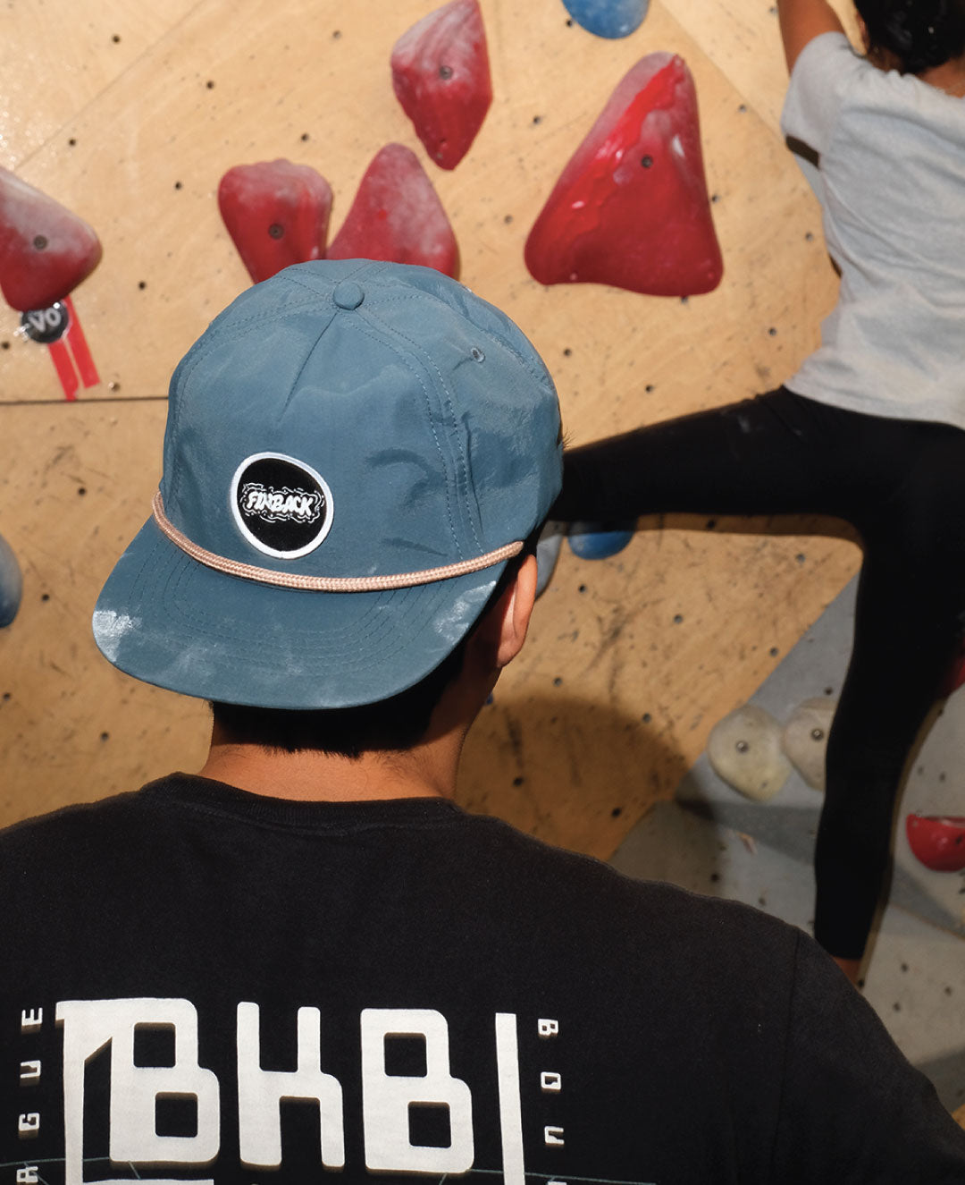 Man in backward hat leads for woman rock climber 